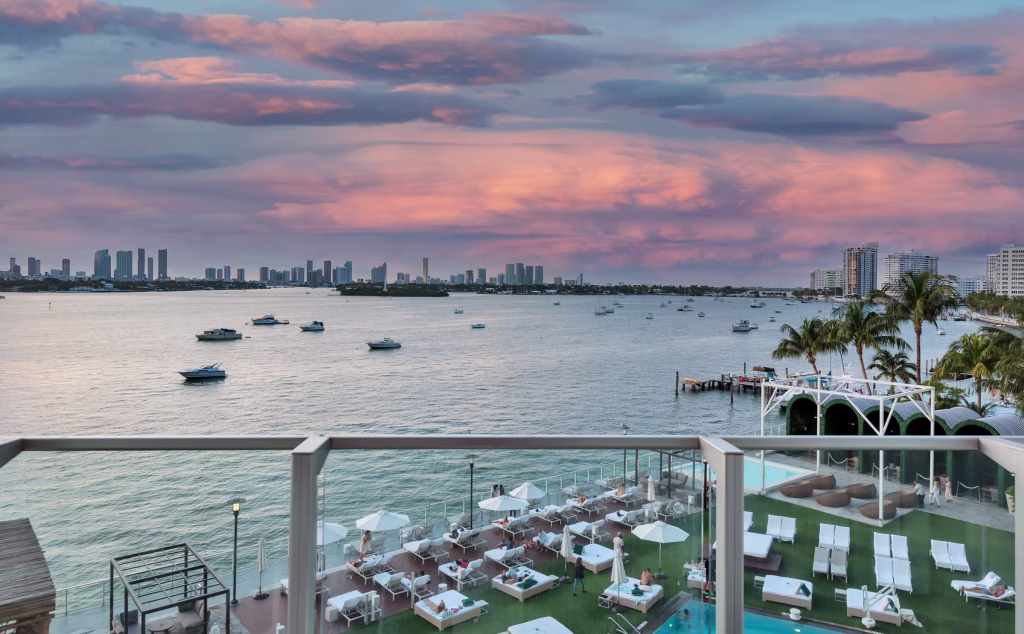 Best way to visit Miami: Balcony and swimming pool at a Miami Beach vacation rental building during sunset, with the city skyline in the background.